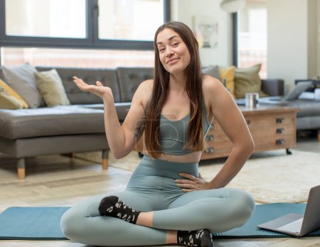 Photo for Young adult woman practicing yoga smiling, feeling confident, successful and happy, showing concept or idea on copy space on the side - Royalty Free Image