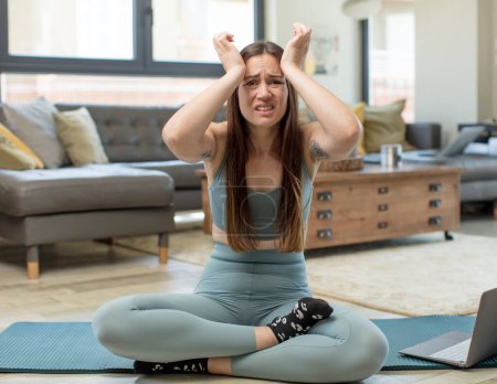 Foto de Mujer adulta joven practicando yoga entrando en pánico sobre un plazo olvidado, sintiéndose estresada, teniendo que encubrir un desorden o error - Imagen libre de derechos