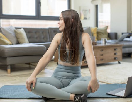 Téléchargez les photos : Jeune femme adulte pratiquant le yoga sur la vue de profil cherchant à copier l'espace devant, penser, imaginer ou rêver - en image libre de droit