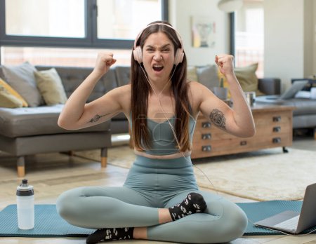 Photo for Young adult woman practicing yoga shouting aggressively with an angry expression or with fists clenched celebrating success - Royalty Free Image