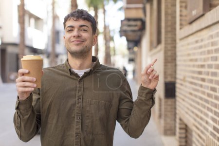 Téléchargez les photos : Jeune bel homme souriant joyeusement, se sentant heureux et pointant vers le côté. concept de café à emporter - en image libre de droit
