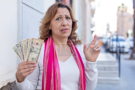 Foto de Mujer bonita de mediana edad cruzando los dedos y esperando buena suerte. concepto de billetes en dólares - Imagen libre de derechos