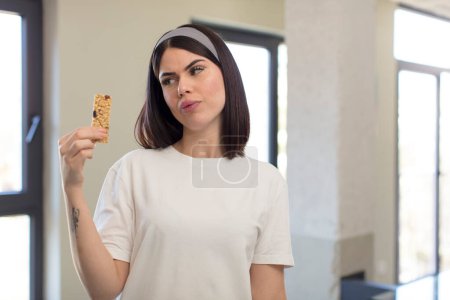 Photo for Pretty young woman smiling and looking with a happy confident expression. fitness cereal bar concept - Royalty Free Image