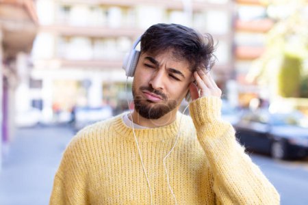 Téléchargez les photos : Jeune homme beau se sentant ennuyé, frustré et somnolent après un fatigant. écouter de la musique avec des écouteurs - en image libre de droit