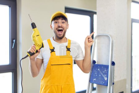 Photo for Young handsome man feeling like a happy and excited genius after realizing an idea. handyman and drill concept - Royalty Free Image