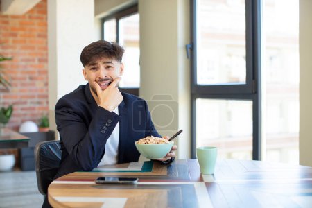 Foto de Joven hombre guapo con la boca y los ojos bien abiertos y la mano en la barbilla. concepto de desayuno - Imagen libre de derechos