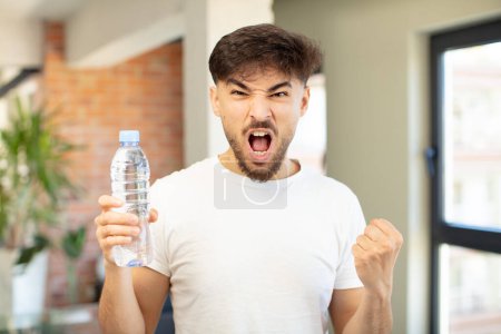 Téléchargez les photos : Jeune homme beau à l'air en colère, agacé et frustré. concept de bouteille d'eau - en image libre de droit