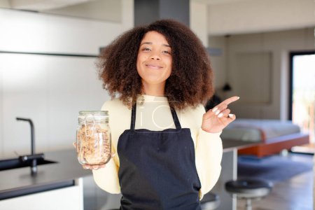 Photo for Pretty afro black woman smiling cheerfully, feeling happy and pointing to the side. homemade cookies concept - Royalty Free Image