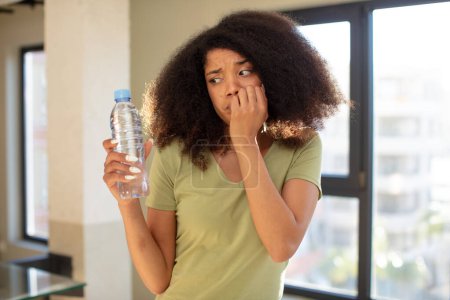 Téléchargez les photos : Jolie femme noire afro se sentant effrayée, inquiète ou en colère et regardant vers le côté. concept de bouteille d'eau - en image libre de droit
