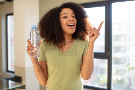 Téléchargez les photos : Jolie afro femme noire se sentant comme un génie heureux et excité après avoir réalisé une idée. concept de bouteille d'eau - en image libre de droit
