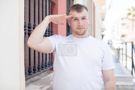 Foto de Hombre guapo saludando a la cámara con un saludo militar en un acto de honor y patriotismo, mostrando respeto - Imagen libre de derechos