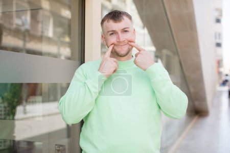 Photo for Handsome man smiling confidently pointing to own fake smile - Royalty Free Image