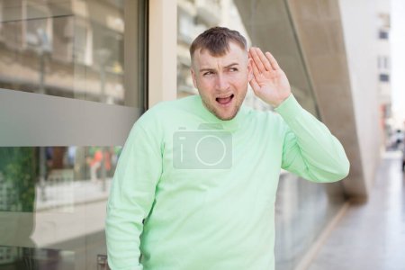 Photo for Handsome man looking happy, listening, trying to hear a secret conversation or gossip, eavesdropping - Royalty Free Image