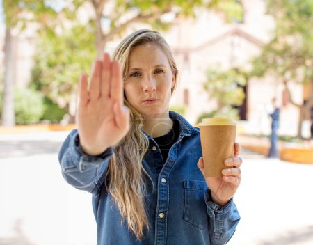 Téléchargez les photos : Regardant sérieux montrant la paume ouverte faisant geste d'arrêt. concept de café à emporter - en image libre de droit
