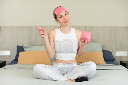 Photo for Smiling cheerfully, feeling happy and pointing to the side. piggy bank concept - Royalty Free Image
