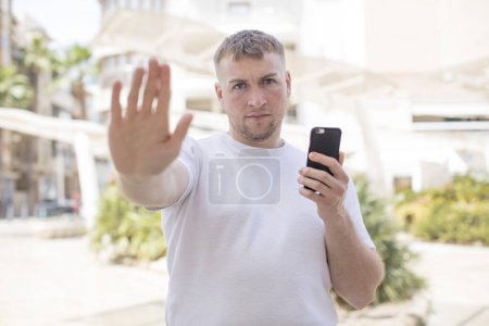 Foto de Mirando seriamente mostrando la palma abierta haciendo gesto de parada. concepto de smartphone - Imagen libre de derechos