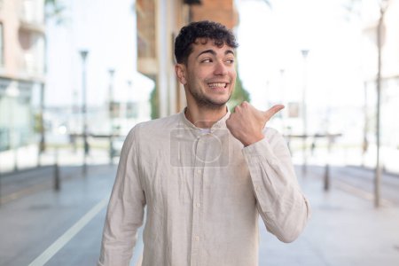 Photo for Young handsome man smiling cheerfully and casually pointing to copy space on the side, feeling happy and satisfied - Royalty Free Image