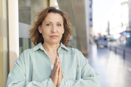 Téléchargez les photos : Femme d'âge moyen se sentant inquiète, pleine d'espoir et religieuse, priant fidèlement avec les paumes pressées, demandant pardon - en image libre de droit