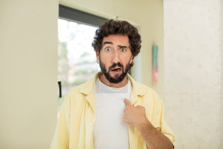 Photo for Young crazy bearded man looking shocked and surprised with mouth wide open, pointing to self - Royalty Free Image
