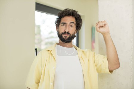 Foto de Joven barbudo loco sintiéndose serio, fuerte y rebelde, levantando el puño, protestando o luchando por la revolución - Imagen libre de derechos