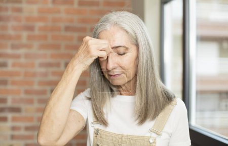 Téléchargez les photos : Senior jolie femme se sentant stressée, malheureuse et frustrée, touchant le front et souffrant de migraine de maux de tête graves - en image libre de droit