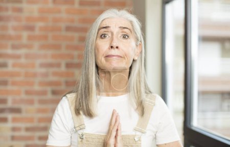 Foto de Anciana bonita mujer sintiéndose preocupada, esperanzada y religiosa, orando fielmente con las palmas presionadas, rogando perdón - Imagen libre de derechos