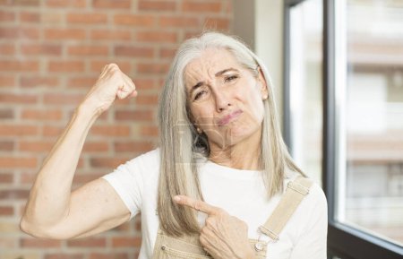 Photo for Senior pretty woman feeling happy, satisfied and powerful, flexing fit and muscular biceps, looking strong after the gym - Royalty Free Image