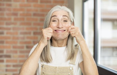 Téléchargez les photos : Senior jolie femme souriant et pointant vers son propre faux sourire - en image libre de droit