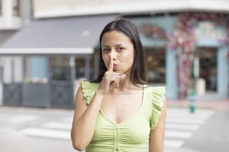 Photo for Pretty hispanic woman looking serious and cross with finger pressed to lips demanding silence or quiet, keeping a secret - Royalty Free Image