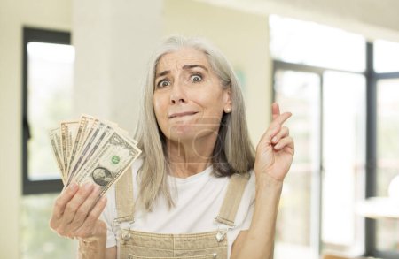 Photo for Pretty senior woman crossing fingers and hoping for good luck. with dollar banknotes - Royalty Free Image