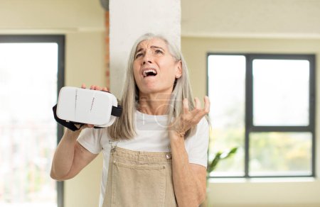 Photo for Pretty senior woman screaming with hands up in the air. with vr goggles - Royalty Free Image