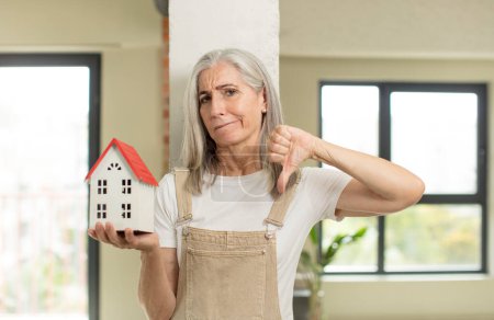 Photo for Pretty senior woman feeling cross,showing thumbs down. with a house model - Royalty Free Image