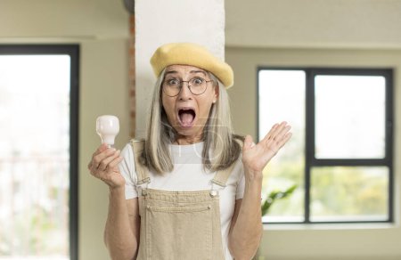 Photo for Pretty senior woman feeling happy and astonished at something unbelievable. with a light bulb - Royalty Free Image