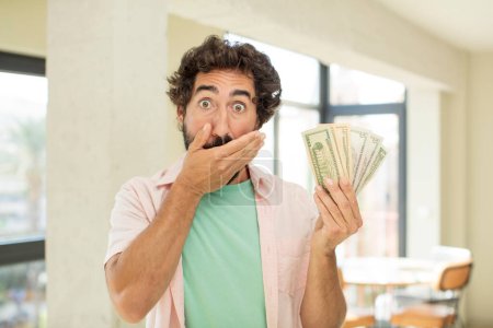 Photo for Crazy bearded man covering mouth with a hand and shocked or surprised expression. dollar banknotes concept - Royalty Free Image