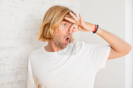 Photo for Young blond adult man feeling disgusted, holding nose to avoid smelling a foul and unpleasant stench - Royalty Free Image