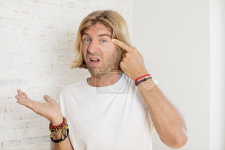 Photo for Young blond adult man feeling confused and puzzled, showing you are insane, crazy or out of your mind - Royalty Free Image