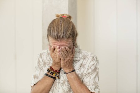 Téléchargez les photos : Jeune homme blond adulte se sentant triste, frustré, nerveux et déprimé, couvrant le visage des deux mains, pleurant - en image libre de droit