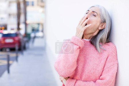 Téléchargez les photos : Senior retraité jolie femme aux cheveux blancs bâillant paresseusement tôt le matin, se réveillant et regardant endormi, fatigué et ennuyé - en image libre de droit