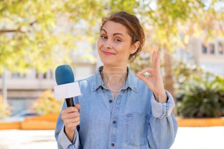 Photo for Young pretty woman feeling happy, showing approval with okay gesture. presenter and microphone concept - Royalty Free Image