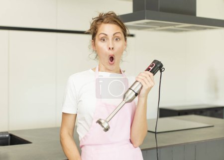 Photo for Young pretty woman feeling extremely shocked and surprised. hand blender concept - Royalty Free Image