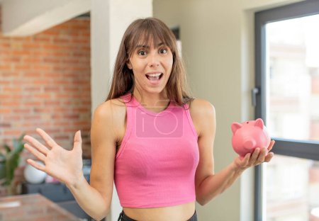 Photo for Young pretty woman feeling happy and astonished at something unbelievable piggy bank concept - Royalty Free Image