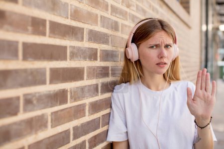 Photo for Young pretty woman looking serious showing open palm making stop gesture. headphones and music concept - Royalty Free Image