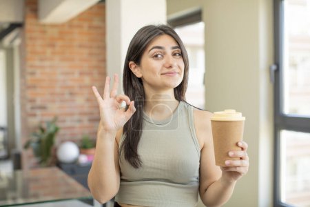 Téléchargez les photos : Jeune femme se sentant heureuse, montrant son approbation avec un geste correct. emporter café - en image libre de droit