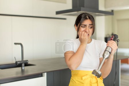 Foto de Mujer joven sintiéndose asustada, preocupada o enojada y mirando hacia un lado. chef con licuadora de mano - Imagen libre de derechos