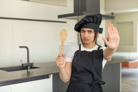 Foto de Mujer joven mirando serio mostrando la palma abierta haciendo gesto de parada. concepto de chef - Imagen libre de derechos