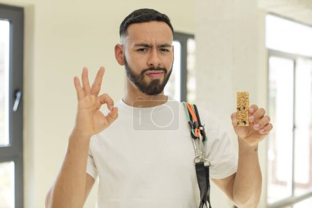 Téléchargez les photos : Bel homme arabe homme arabe se sentant heureux, montrant son approbation avec un geste correct. concept de barre de fitness et de céréales - en image libre de droit