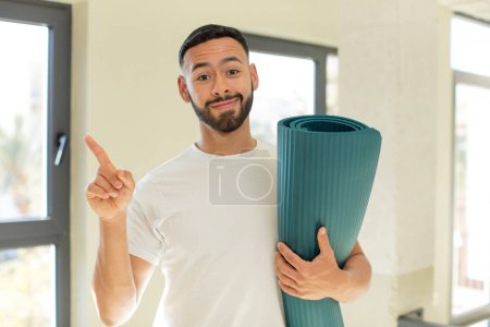 Téléchargez les photos : Homme beau arabe homme arabe souriant joyeusement, se sentant heureux et pointant vers le côté. yoga concept mat - en image libre de droit