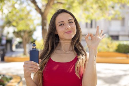 Photo for Pretty woman feeling happy, showing approval with okay gesture. vaper concept - Royalty Free Image
