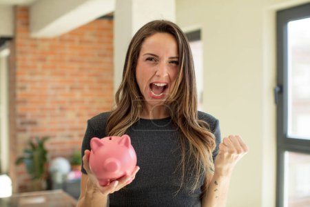 Photo for Pretty woman looking angry, annoyed and frustrated. piggy bank - Royalty Free Image