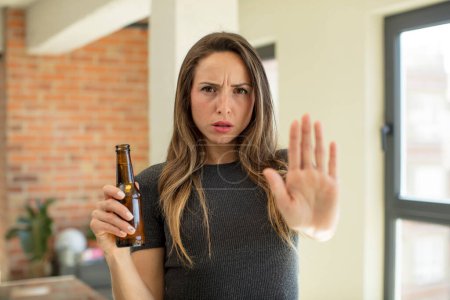 Photo for Pretty woman looking serious showing open palm making stop gesture. beer bottle - Royalty Free Image
